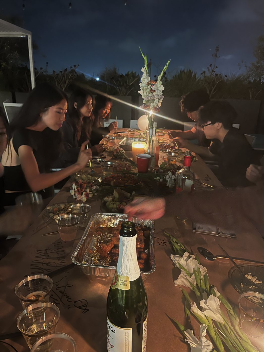 Guests around the long candlelit table, drawing on the paper and eating